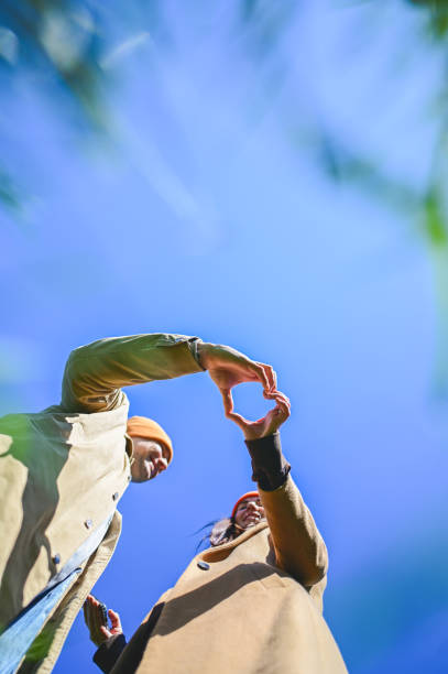 Young couple making heart shape with hands against blue sky