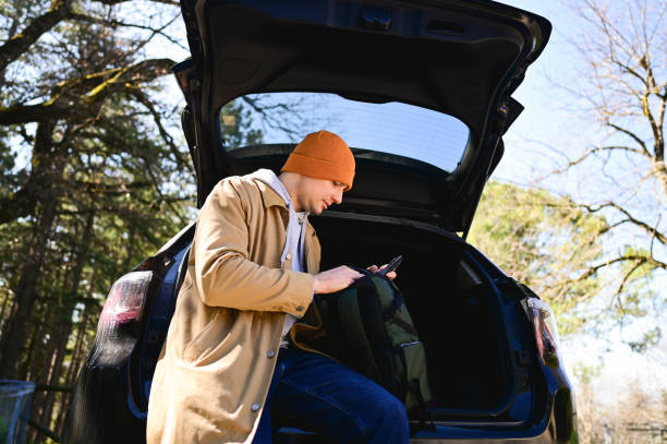 istock Tourist using smartphone while sitting in car trunk in forest 2206041119