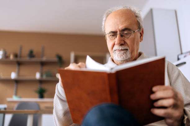 istock Senior man reading a book while sitting in an armchair at home 2206044903