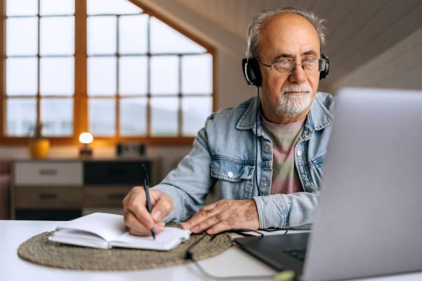 istock Senior man with headphones working from home and taking notes 2206044921
