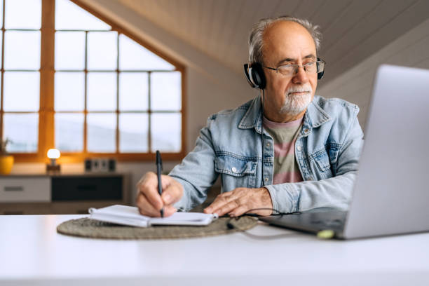 istock Senior man with headphones working from home and taking notes 2206045052