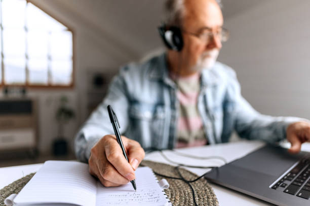 istock Senior man with headphones working from home and taking notes 2206045147