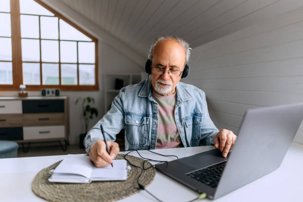 istock Senior man with headphones working from home and taking notes 2206045230