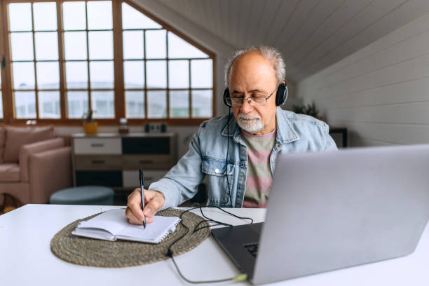 istock Senior man with headphones working from home and taking notes 2206045309