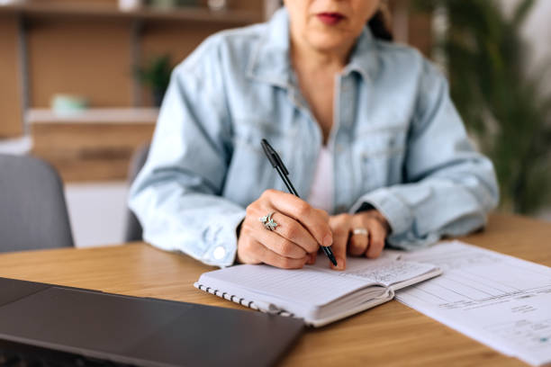 istock Close up shot of senior woman writing notes while using a laptop at home 2206045342