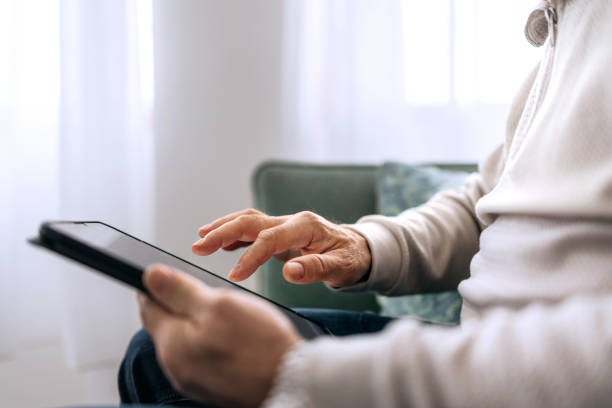 istock Close-up of a senior man using a digital tablet on the sofa at home 2206045403