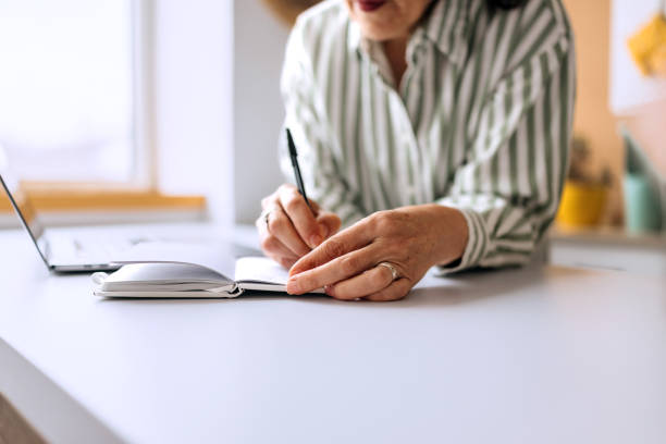 istock Close up shot of senior woman taking notes while working from home 2206045440