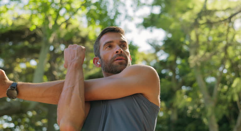Outdoor, athlete and man with earphones, stretching and listening to music for fitness and serious. Routine, training and warm up for person in nature, performance or workout with playlist in morning