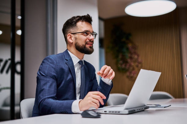 istock Businessman working on laptop in modern office, looking away and smiling 2206047330