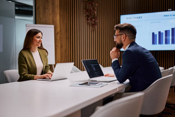 Business people working together on laptops in modern office meeting room analyzing bar chart