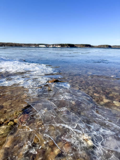 Cracked ice on a rocky shore of a thawed lake under a bright spring blue sky. A contrast of melting cold and warm seasonal renewal