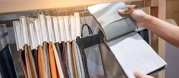 istock Designer hand choosing fabric pieces from fabric swatch material. Upholstery sample collection hanging on showcase rack. Textile industry for home interior design and furniture finishing decor 2206051665