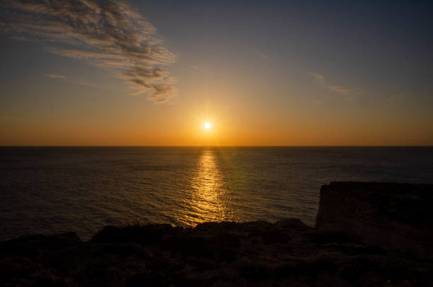A stunning sunset over the vast ocean, casting golden hues across the sky and water. The suns reflection creates a peaceful and serene atmosphere.