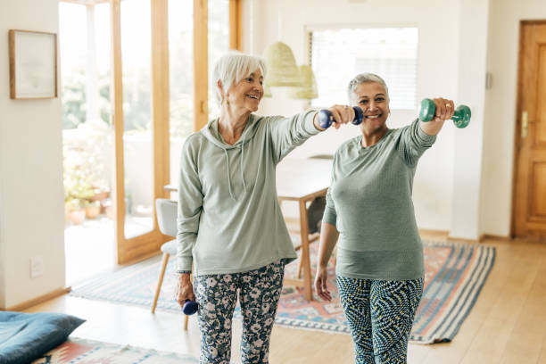 Stronger Every Day: Senior Women Lifting Weights Two mature women practicing resistance training at home, embracing an active and healthy lifestyle. osteoporosis stock pictures, royalty-free photos & images
