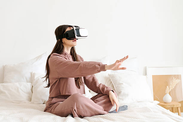 istock Woman is sitting on a bed wearing a VR headset 2206062467