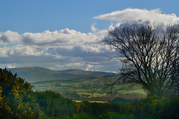 Sunlight through clouds casts shadows on the Sperrin Mountains seen from a distance looking south from Ervey Cross