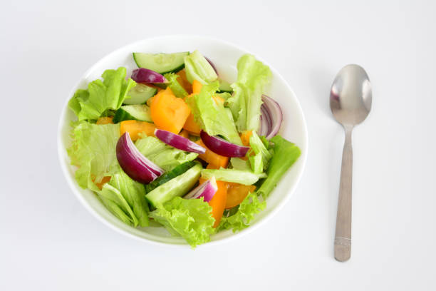 Fresh and healthy salad with mixed vegetables in a white bowl next to a spoon