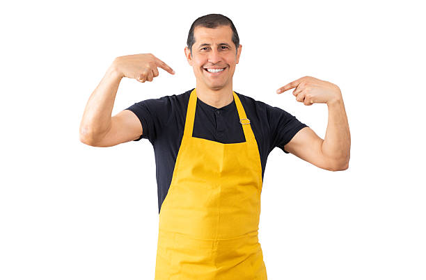 Salesman with yellow apron over white isolated background looking confident with smile on face, pointing oneself with fingers proud and happy.