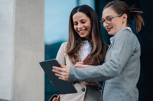 istock Two businesswomen smiling and using a digital tablet outside office building 2206073087