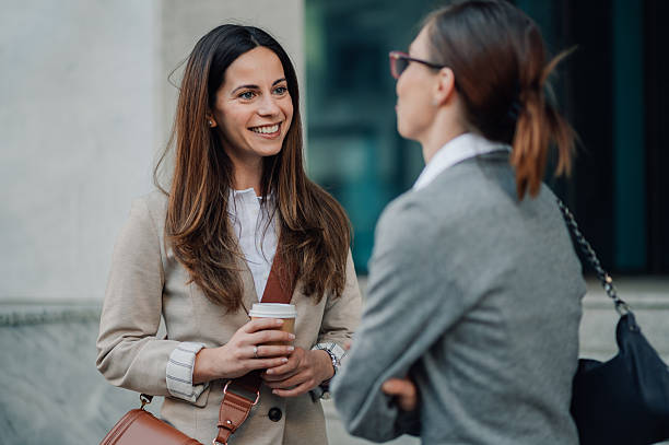 istock Two businesswomen talking and smiling outdoors while holding a coffee 2206073115
