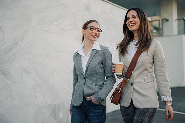 Two businesswomen walking and talking outdoors with coffee