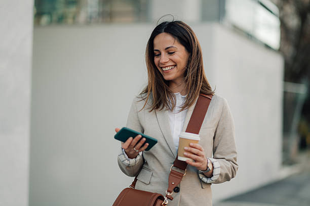 istock Smiling businesswoman walking and using smartphone while holding coffee 2206073629