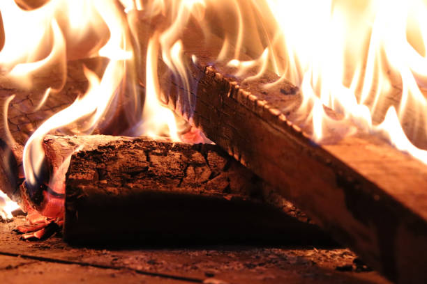 A close-up that captures firewood burning inside a traditional pizza oven. The flames dance around the logs, creating a warm, golden glow that illuminates the textured bricks of the oven. The intense heat radiates from the fire, emphasizing the rustic and cozy ambiance of an authentic wood-fired oven.