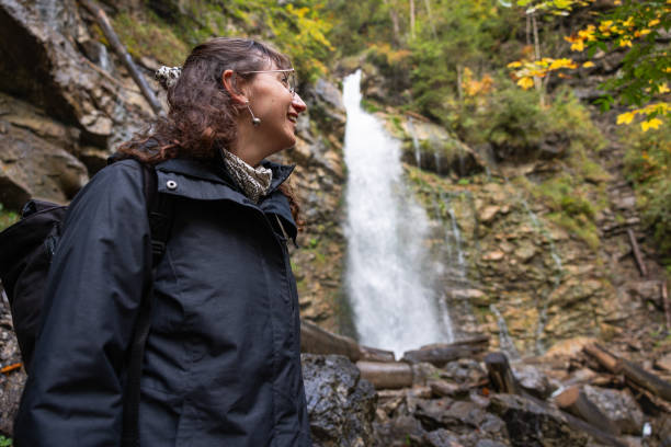 Woman in hiking gear exploring a waterfall in the Austrian Alps on a rainy day during autumn