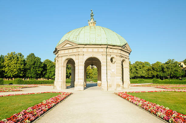 Munich, Germany, 7th of August 2024 - Pathway lined with purple and white flowers leads to the grand Nymphenburg Palace, Munich, under a vibrant sky