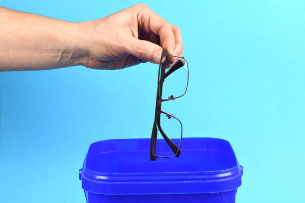 istock Hand holding plastic black glasses puts in blue container, isolated on white background. 2206093517