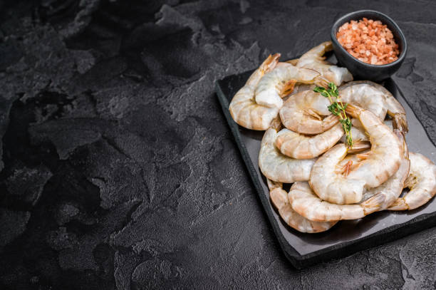 istock Raw headless white shrimps prawns on a marble board. Top view. Black background 2206095262