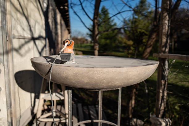 A circular metal basin on a stand with a power tool resting on it, surrounded by an outdoor rural setting featuring natural elements and wooden structures.