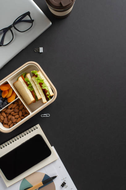 A top view of a desk setup showing a laptop, glasses, lunchbox, notebook, and coffee cup, creating a productive and organized environment ideal for work or study