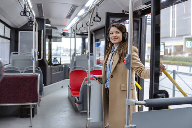 istock Smiling woman boarding a bus while holding a smartphone 2206107779
