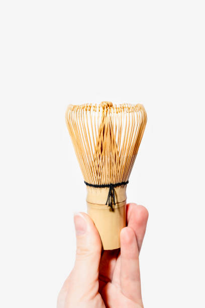 Hand Holding Traditional Bamboo Matcha Whisk Against White Background
