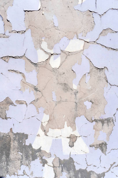 Peeling paint reveals textured layers on a weathered wall in an urban setting during daylight hours