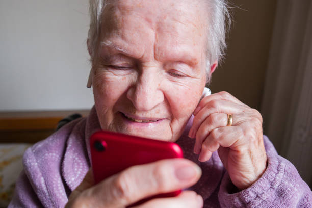 istock Elderly woman using red smartphone and wireless earbuds at home 2206116182