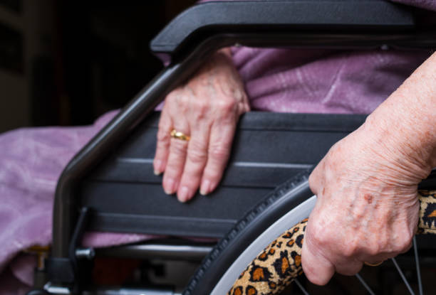 Close up of wrinkled hands of elderly female patient using leopard animal-print custom wheelchair, representing mobility and independence in old age