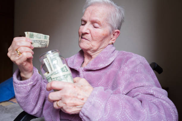 Senior woman carefully placing dollar bills into a glass jar, managing savings and pension funds to meet her expenses while navigating the challenges of retirement living