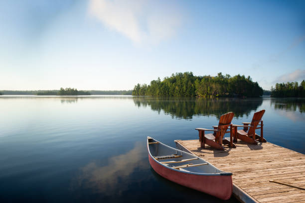 стокові фото, фото роялті-фрі та зображення на тему крісла adirondack на причалі muskoka з каное та видом на озеро. - озеро