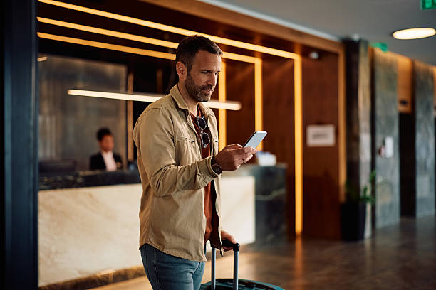istock Man with travel bag texting on mobile phone while arriving at the hotel. 2206124139