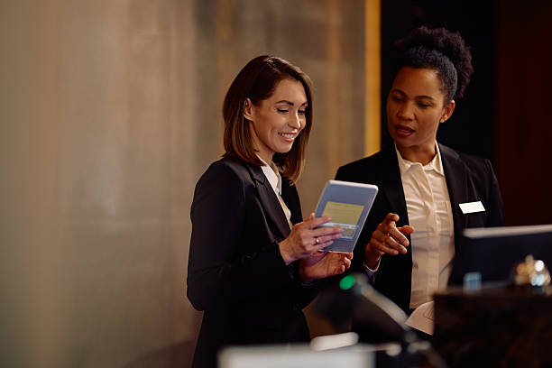 female hotel receptionists using digital tablet while working at front desk. - trabalho em hotelaria imagens e fotografias de stock