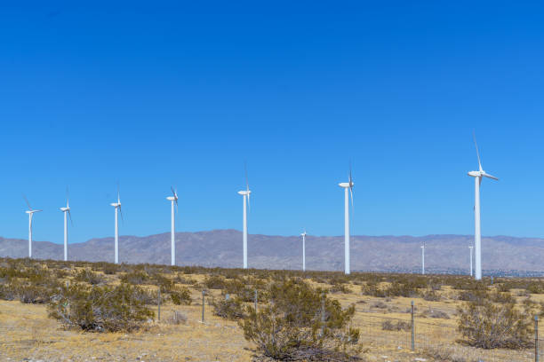 A line of white wind turbines stands in a desert landscape under a clear blue sky in Palm Springs with copy space.