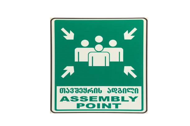 Emergency assembly point sign showing people icons and leading arrows, designed to guide individuals to designated safe areas during evacuations or emergencies.