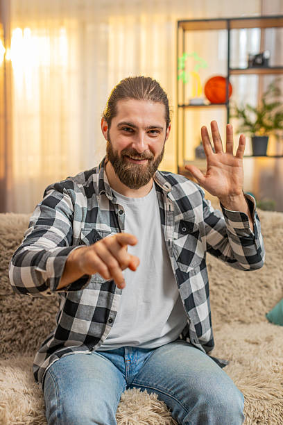 istock Cheerful young man greeting sits on home sofa wave hey you hello, inviting, optimism, bright gesture 2206127272