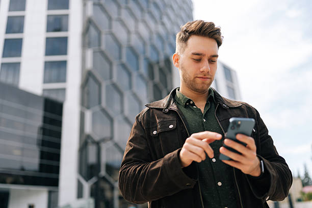 istock Low-angle portrait of focused successful business man using smartphone outside modern office center, confidently engaging in business communication on mobile app 2206127376
