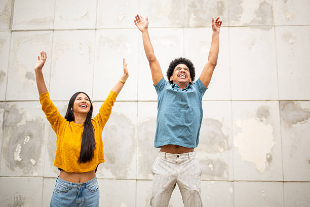 cheerful young couple standing by wall with hands raised