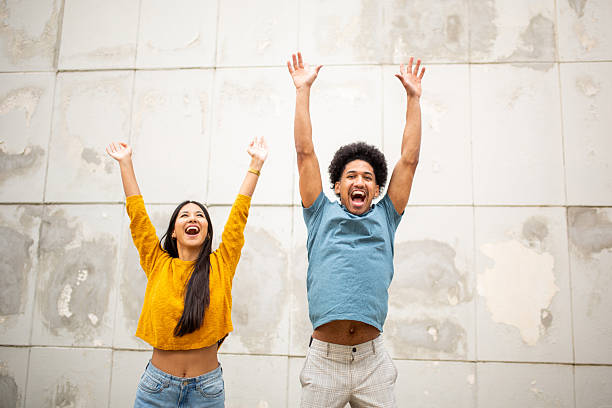 istock happy young couple standing by wall with arms raised 2206127521