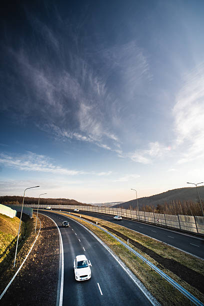 Cars traverse a winding highway surrounded by open fields and an expansive sky, creating a sense of freedom and exploration.