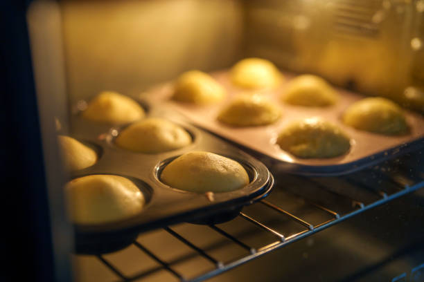 Golden muffins baking in a hot oven, rising beautifully in their trays. The warm glow highlights the fluffy texture of the homemade batter, capturing the essence of home baking.